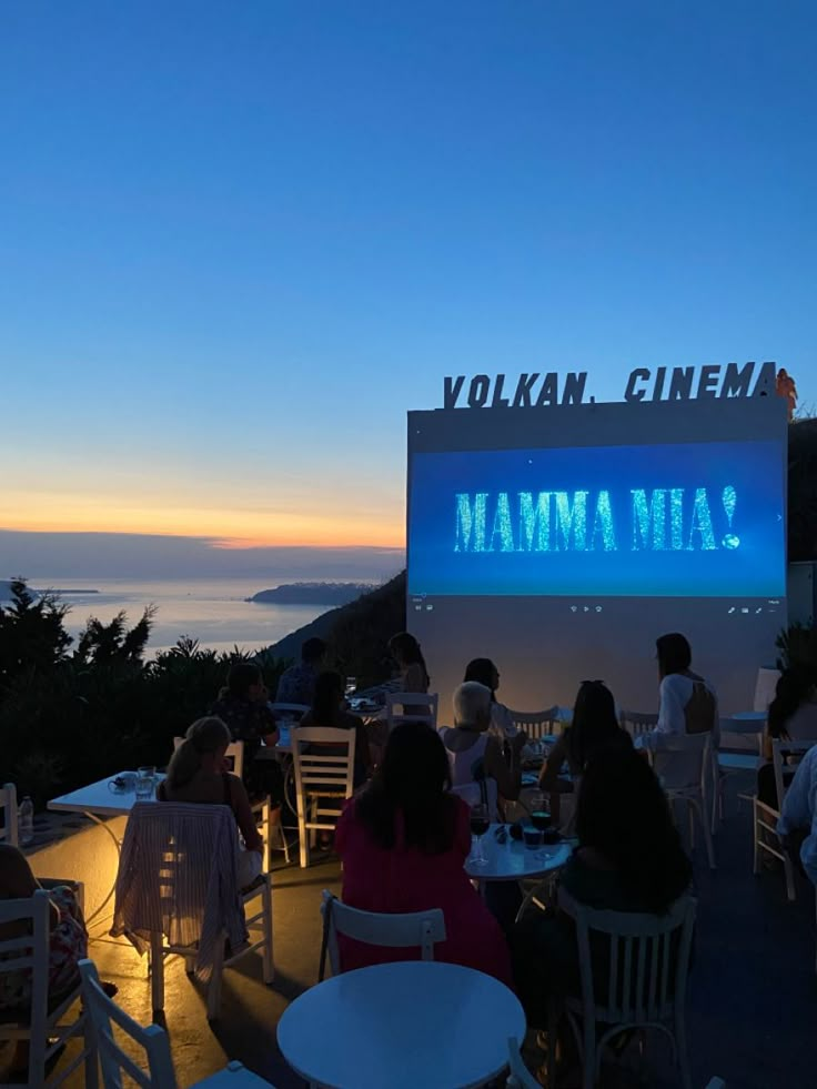 people sitting at tables in front of a movie screen with the ocean in the background