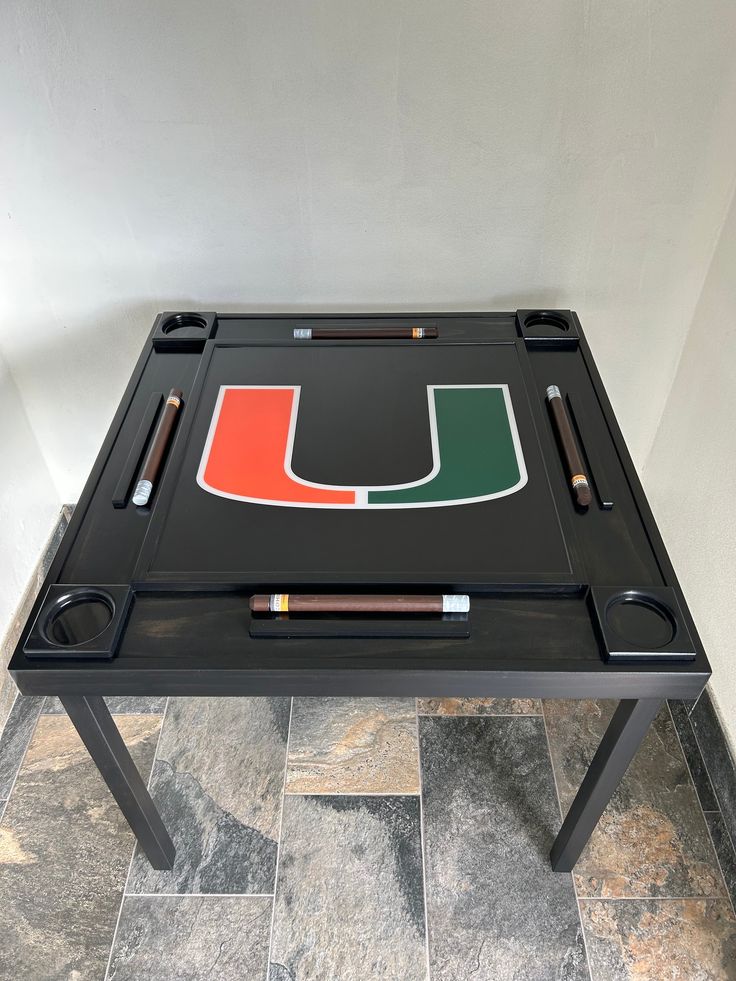 the university of miami game table is made out of black metal and has a red, green, and orange logo on it