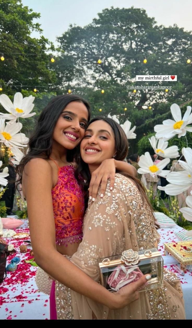 two women hugging each other in front of flowers