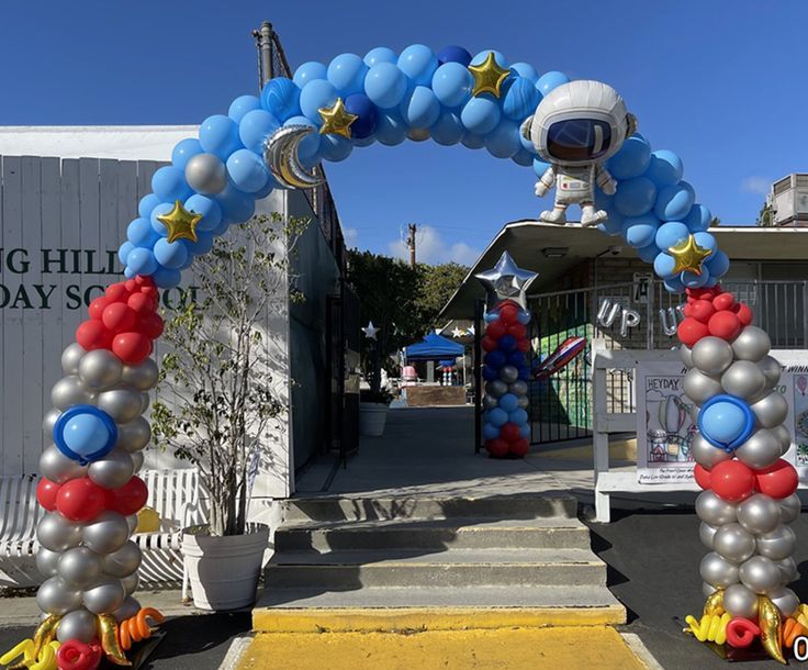 an astronaut balloon arch is decorated with blue, red and silver balloons in front of a building