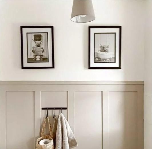 two pictures hang on the wall above a towel rack with towels and other items in front of it