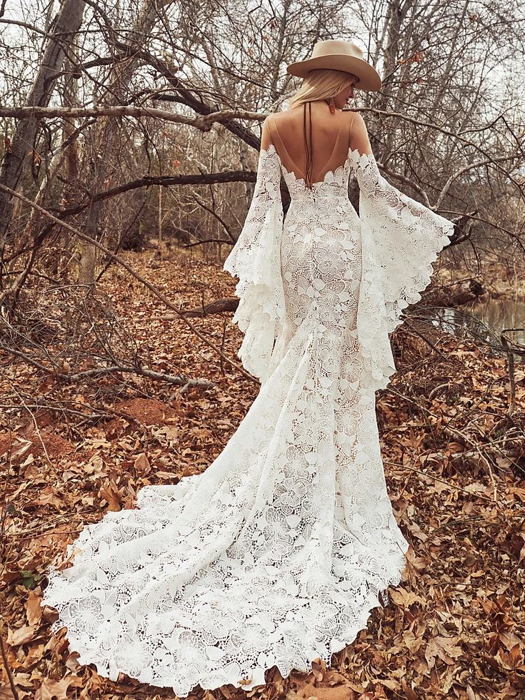 a woman in a white dress and hat standing in leaves with her back to the camera