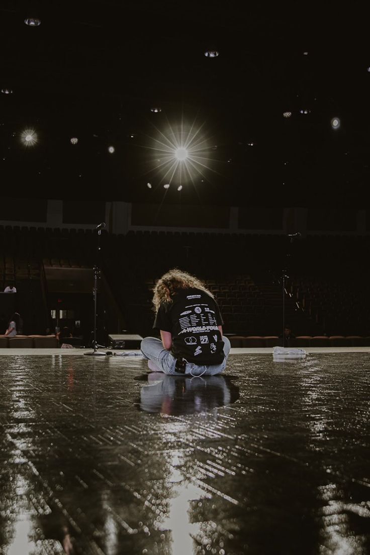 a person sitting on the floor in front of a basketball court with lights shining down