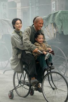 a man and woman riding on the back of a bike with a child in it