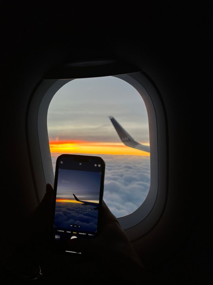 a person taking a photo of an airplane wing with their cell phone in front of the window