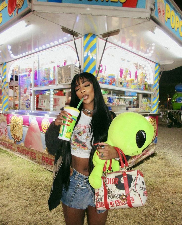 a woman standing in front of a food stand holding a drink and a stuffed animal