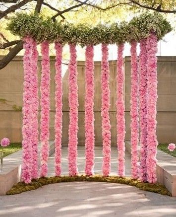 an outdoor ceremony with pink flowers and greenery hanging from the ceiling, in front of a tree