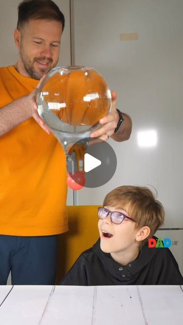 a man is holding up a fish bowl to a young boy who is sitting at a table