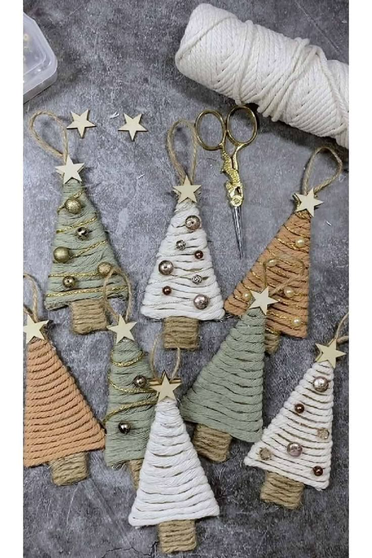 knitted christmas tree ornaments with gold stars hanging from hooks on a gray surface next to a ball of twine