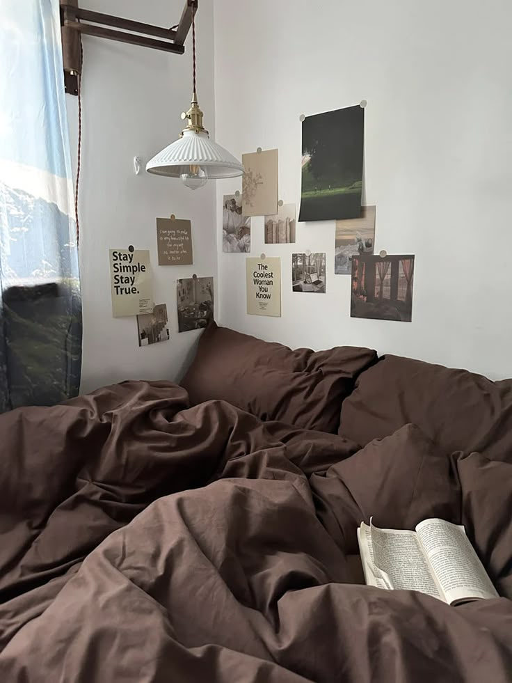 an unmade bed with brown sheets and pictures on the wall above it, along with a lamp