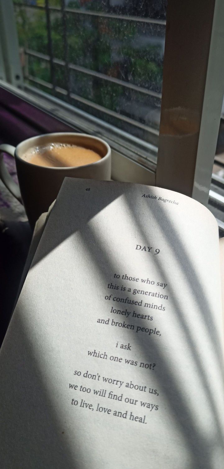 an open book sitting on top of a table next to a cup of coffee and a window