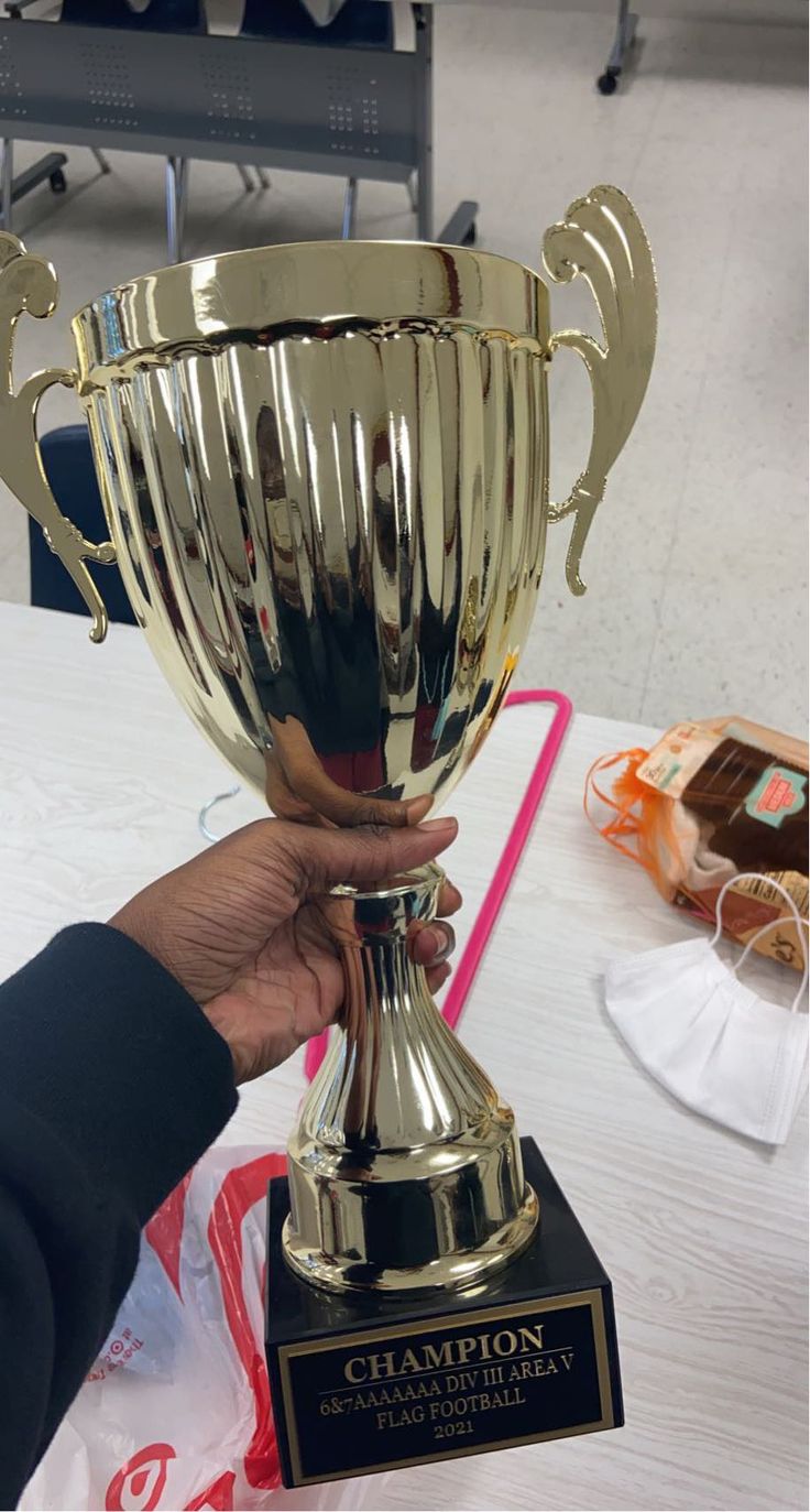 a person holding up a large trophy on top of a white tablecloth covered table