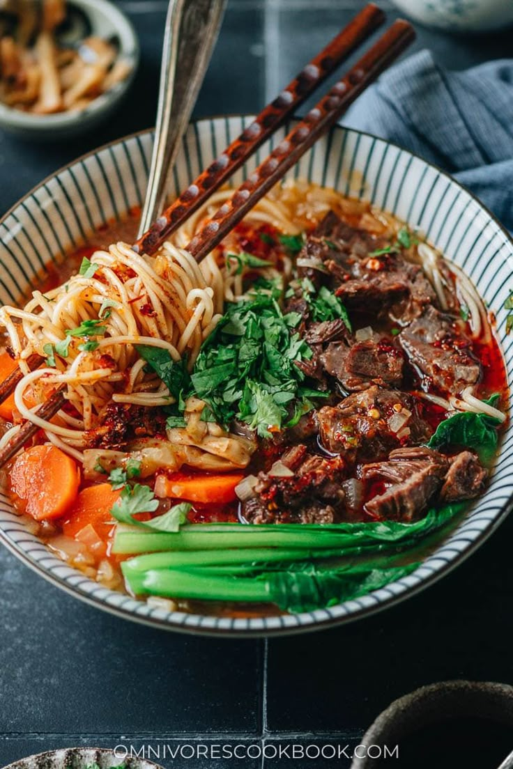 a bowl filled with noodles, meat and veggies next to chopsticks