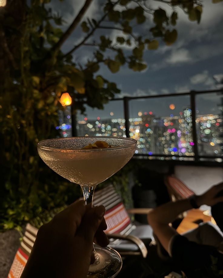 a person holding a wine glass with a view of the city lights in the background