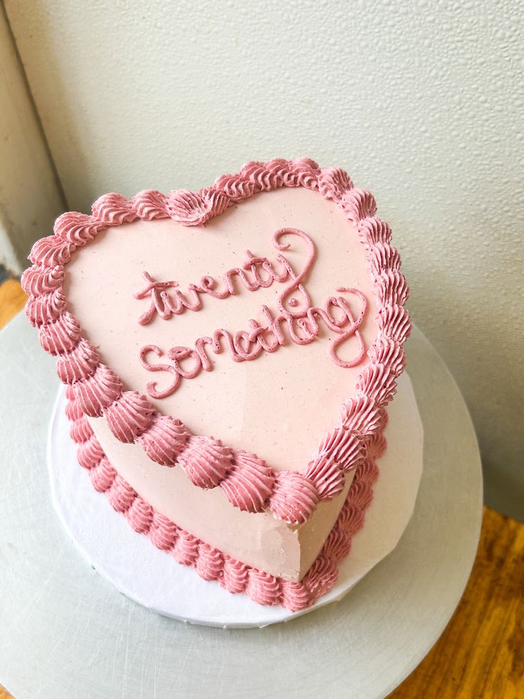 a heart shaped cake sitting on top of a white plate with pink frosting and writing