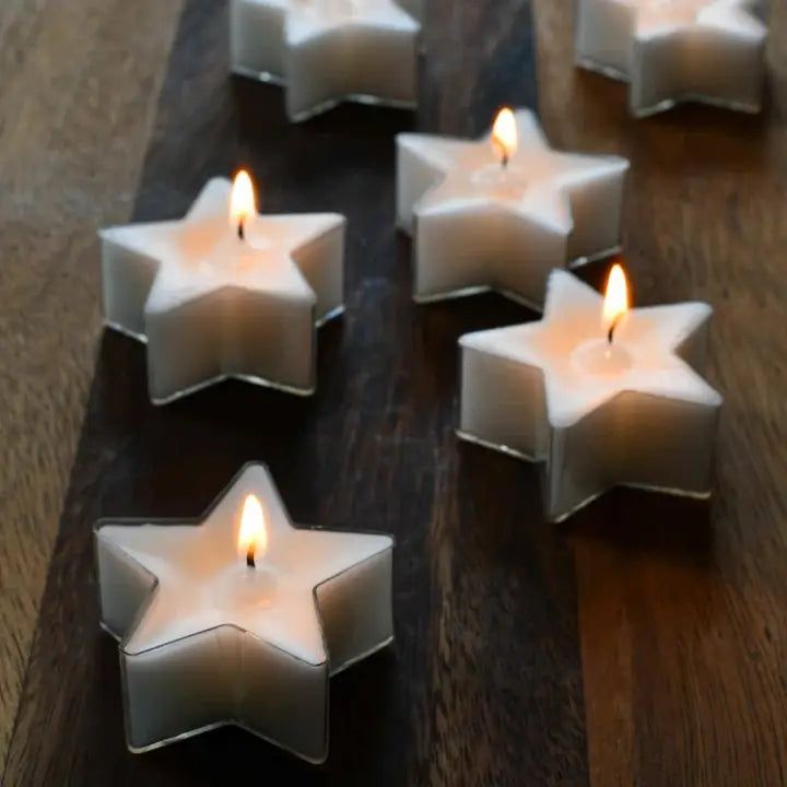 many white candles are arranged in the shape of stars on a wooden table with one candle lit