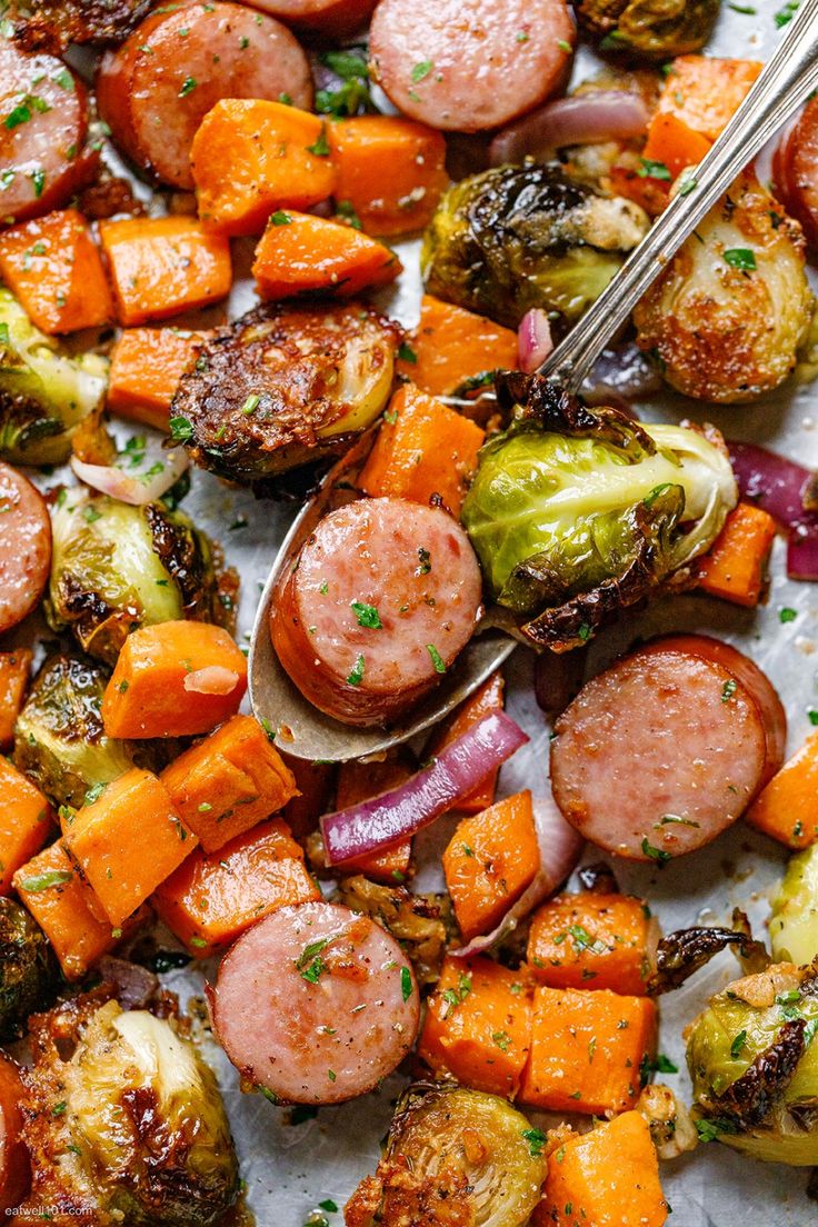 sausage, potatoes and brussels sprouts on a sheet of parchment paper with tongs