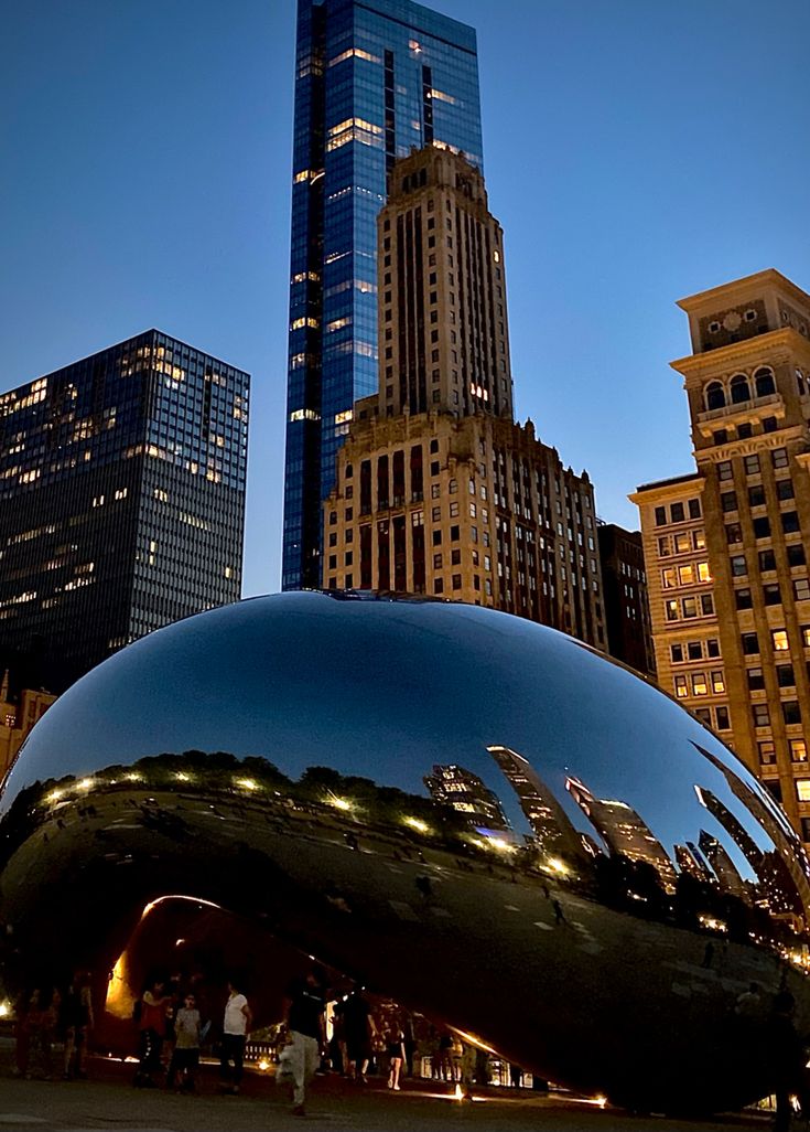 a large metal sculpture in the middle of a city at night with skyscrapers behind it