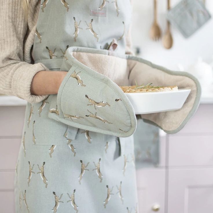 a woman in an apron holding a plate with food on it and wearing a mitt