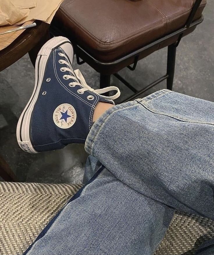 a person sitting on a chair with their legs crossed and wearing blue converse shoes,