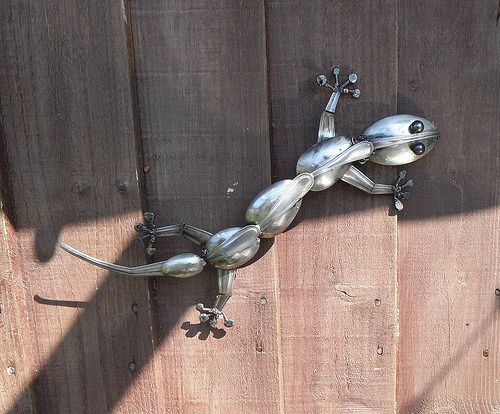 a metal lizard sitting on top of a wooden fence