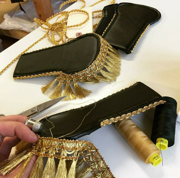 a pair of black shoes being sewn with gold tassels and thread on the table