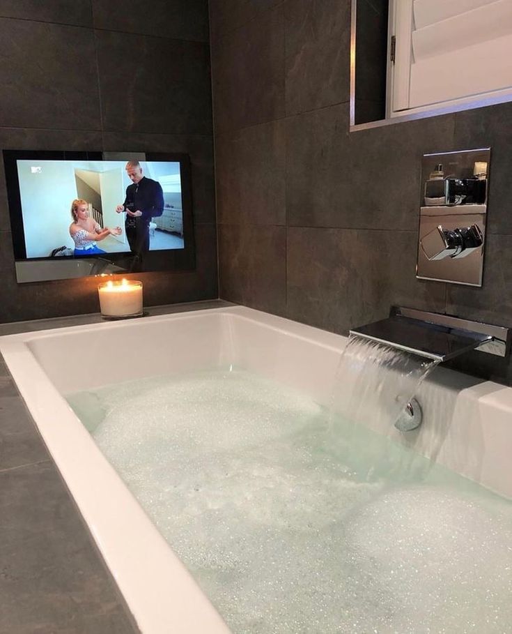 a bathtub with water running from the faucet in front of a tv