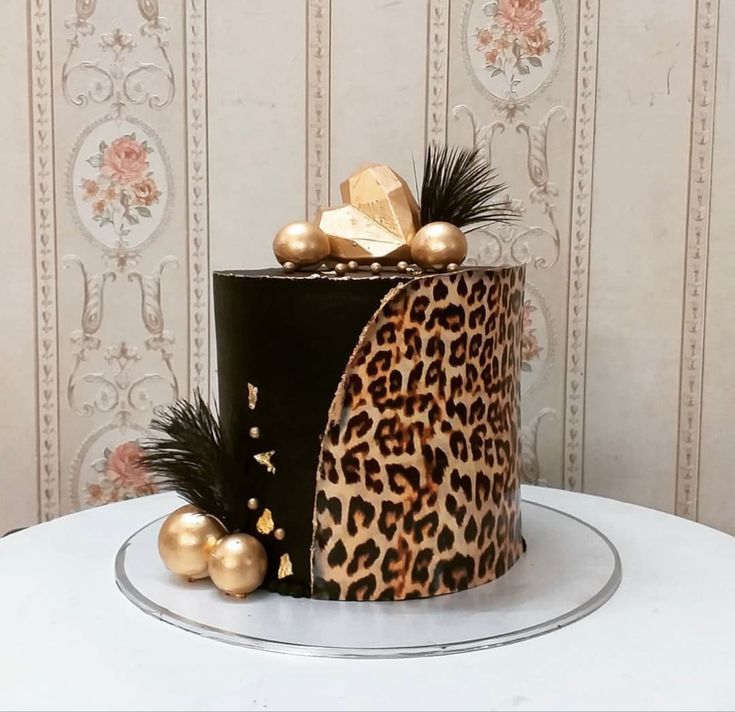 a leopard print cake with gold decorations and feathers on the top, sitting on a white table