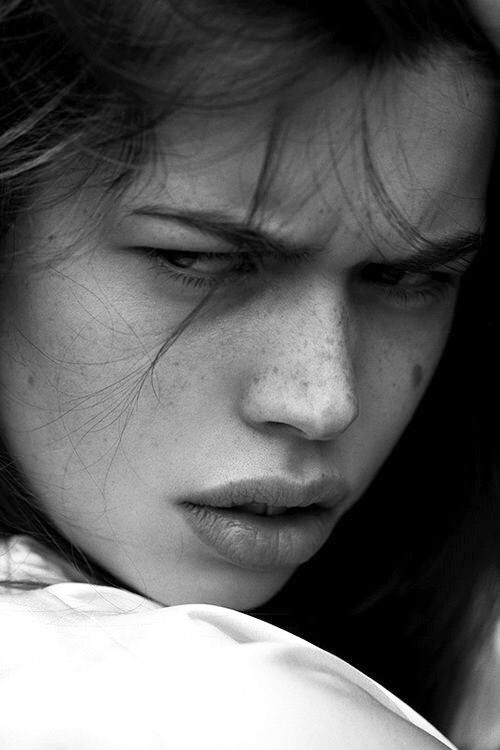 a black and white photo of a woman with freckles on her face looking down