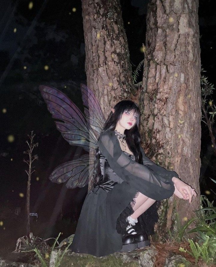 a fairy sitting on the ground next to a tree