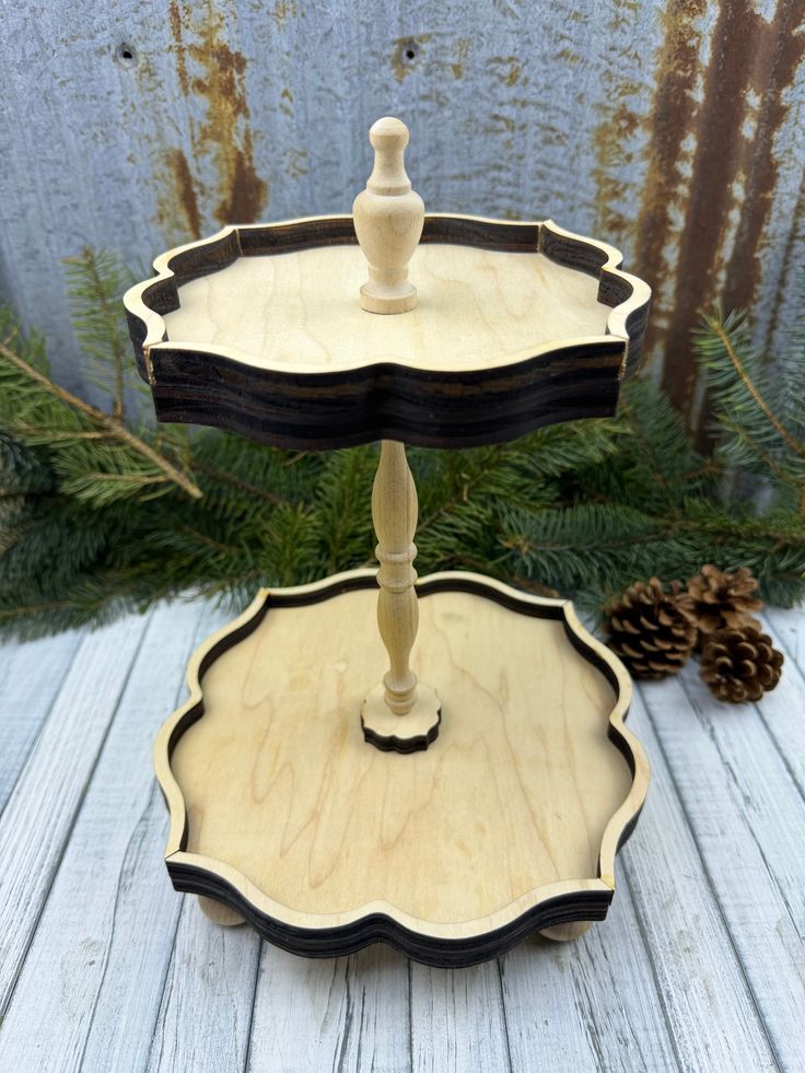 two tiered serving tray with pine cones on the side and evergreen branches in the background