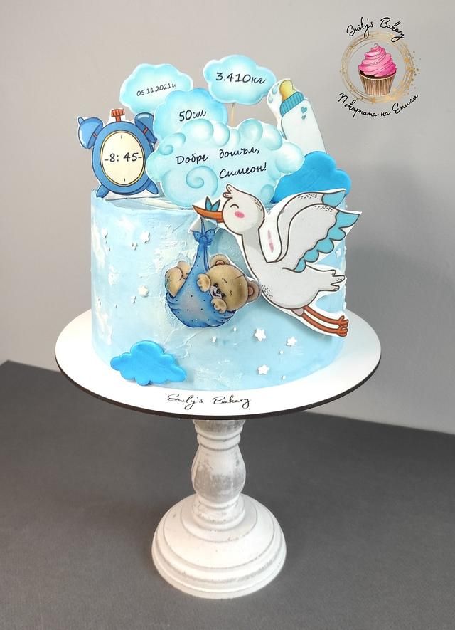 a baby shower cake with blue icing and white frosting on a pedestal in front of a gray wall