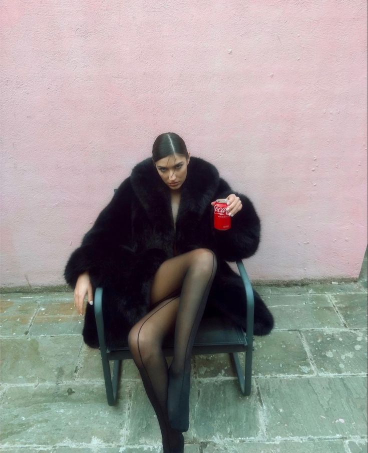 a woman sitting in a chair with her legs crossed, holding a cup and wearing tights