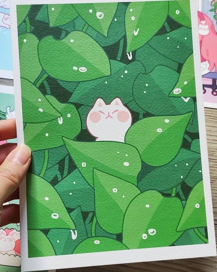 a hand holding up a card with an image of a cat in the middle of green leaves