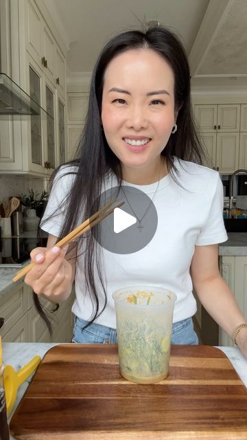 a woman holding chopsticks in front of a glass on top of a cutting board