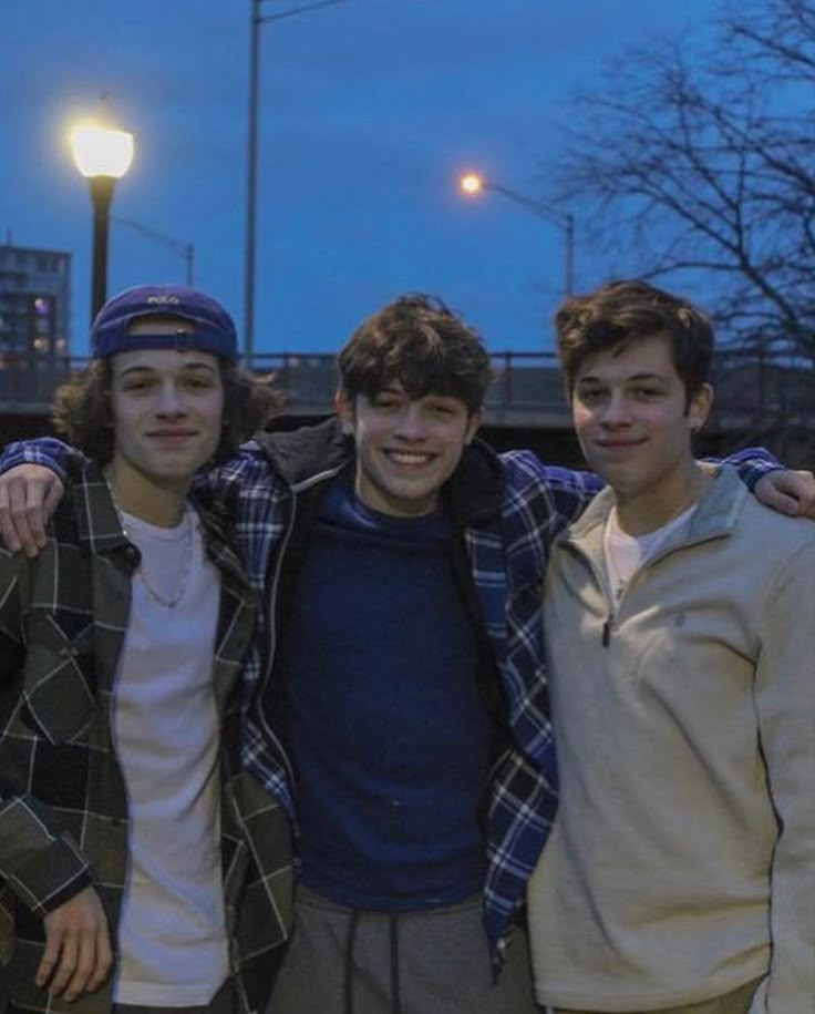 three young men standing next to each other in front of a street light at night