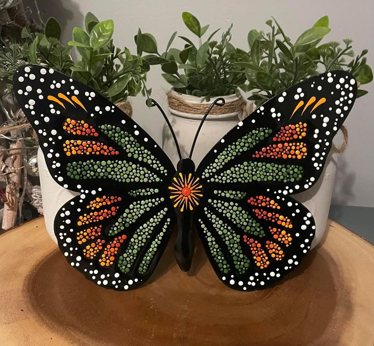 a painted butterfly sitting on top of a wooden table next to a potted plant