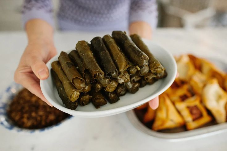 a person holding a plate with some food on it and other foods in the background