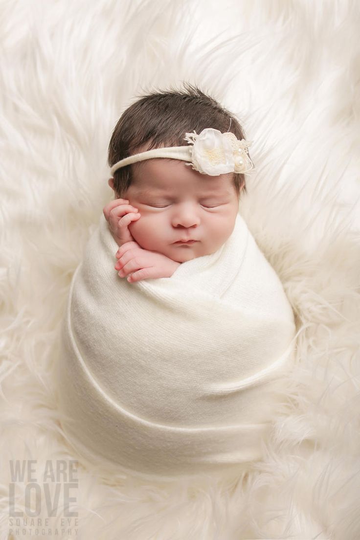 a newborn baby is wrapped in a white blanket with a flower on it's head