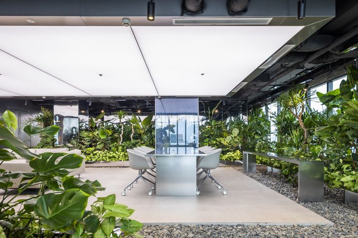 an office with plants and chairs in the center, surrounded by greenery on both sides