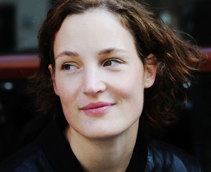 a close up of a person wearing a black jacket and smiling at the camera with her hair blowing in the wind