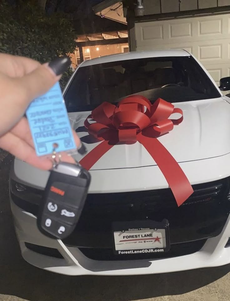 a car with a red ribbon and a tag attached to the hood is parked in front of a house