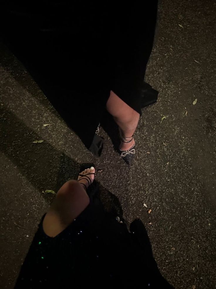 a woman in high heels standing on the street at night with her legs crossed and one foot up