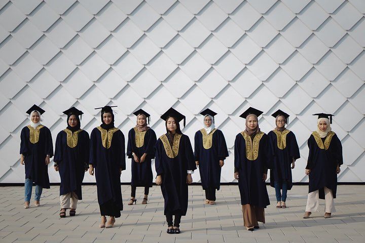 a group of people in graduation gowns and caps walk together on a sidewalk near a wall