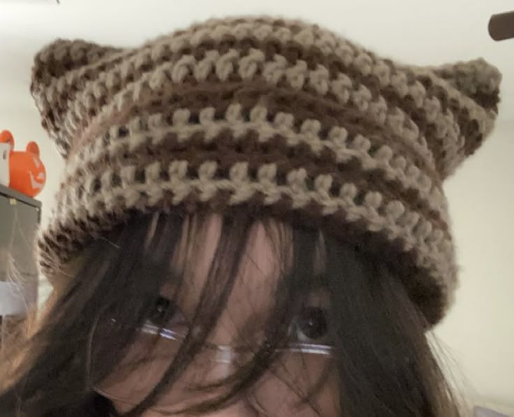 a close up of a person wearing a knitted hat with glasses and a cell phone in the background