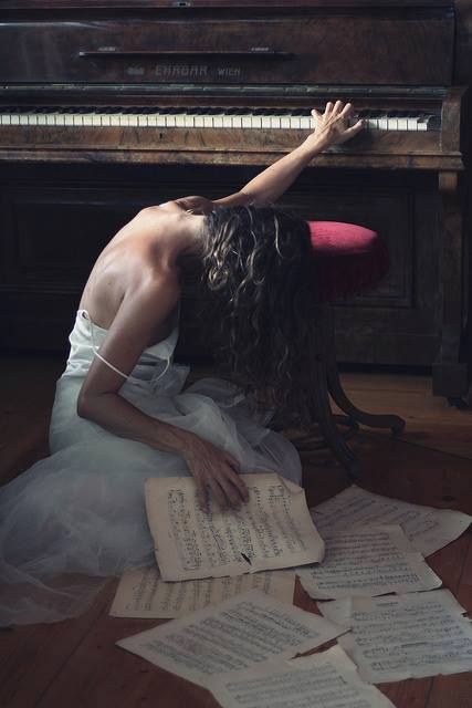 a woman sitting on the floor in front of a piano with sheets of paper around her