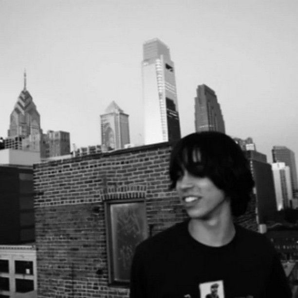 a young man standing in front of a brick building with the city skyline behind him