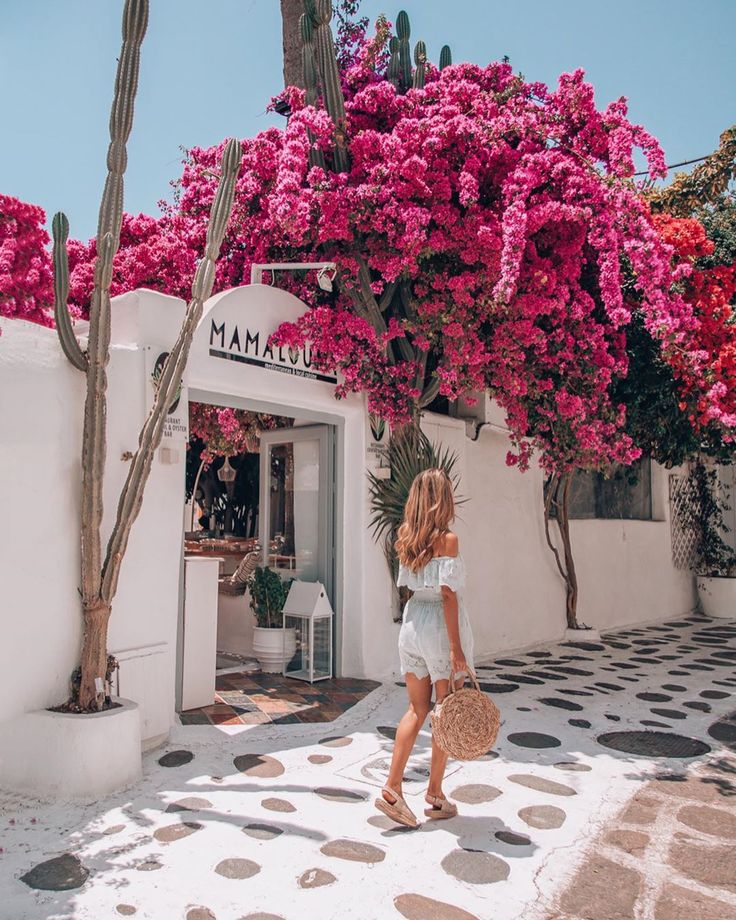 a woman walking down the street in front of a building with pink flowers on it