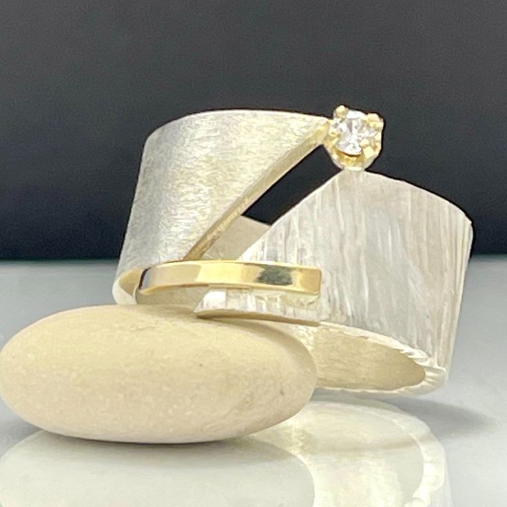 a gold and silver ring with a diamond on it's center, sitting on top of a rock