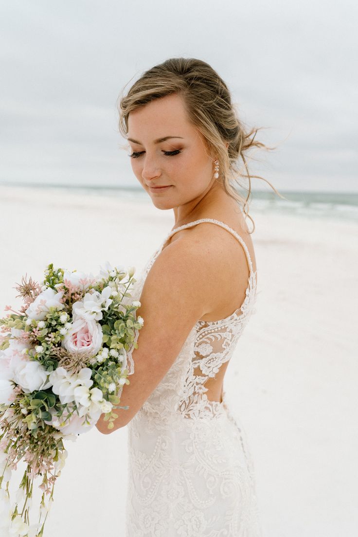 a woman in a wedding dress holding a bouquet on the beach